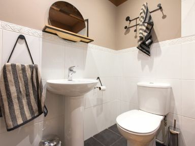 A bathroom with a pedestal sink, toilet, round mirror, towel racks, and striped towels at The Bolthole in Eglingham