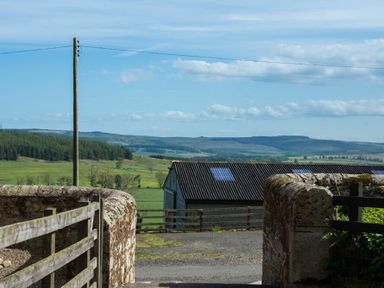 A rural landscape with a wooden gate stone walls barn and hills in the background at The Bolthole in Eglingham