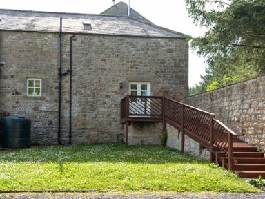 A stone building with wooden stairs and railing leading to a door at The Bolthole in Eglingham
