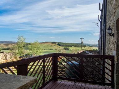 A balcony with wooden railing overlooking fields and hills at The Bolthole in Eglingham