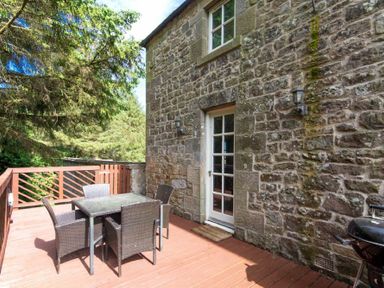 A wooden deck with a table and four chairs outside a stone house at The Bolthole in Eglingham