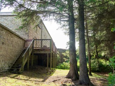 A wooden deck with stairs attached to a stone building in a grassy area with trees at The Bolthole in Eglingham
