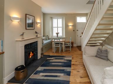 A living room with a fireplace a sofa stairs and a dining table at Strandline in Alnmouth