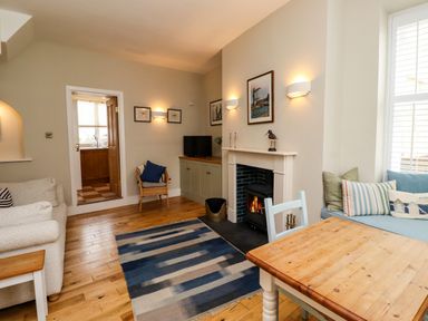 A living room with a fireplace a wooden table sofa armchair and a blue rug at Strandline Alnmouth