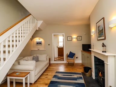 A living room with a sofa under stairs a wood burning stove and a doorway to a kitchen at Strandline in Alnmouth