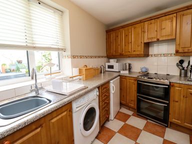 A kitchen with wooden cabinets a washing machine a microwave and a stove at Strandline Alnmouth
