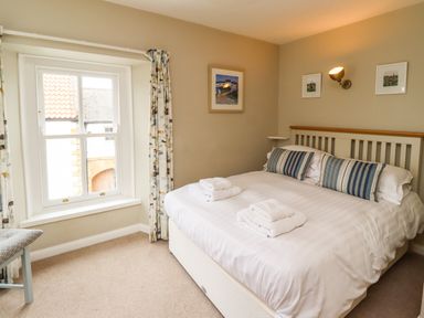 A bedroom with a bed with striped pillows and two sets of folded towels on top next to a window with patterned curtains at Strandline in Alnmouth