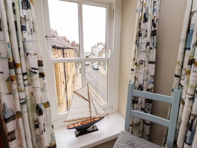A window with patterned curtains a model sailboat on the windowsill and a chair with a patterned cushion at Strandline in Alnmouth