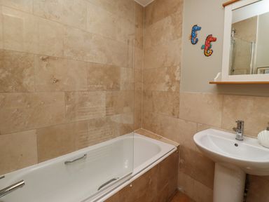A bathroom with a bathtub sink and wall tiles at Strandline in Alnmouth