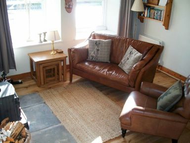 A living room with two leather chairs a wooden side table with a lamp and a woven rug at Swallow Cottage nr Powburn in Powburn