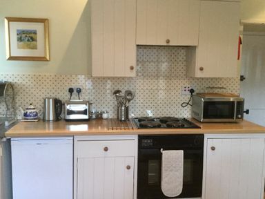 A kitchen with white cabinets a black oven a microwave kettle toaster and a framed picture on the wall at Swallow Cottage nr Powburn in Powburn