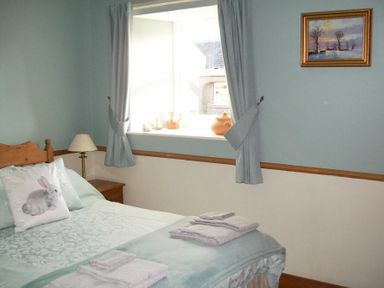 A bedroom with a bed a pillow with a rabbit image a nightstand and a window with blue curtains at Swallow Cottage nr Powburn in Powburn