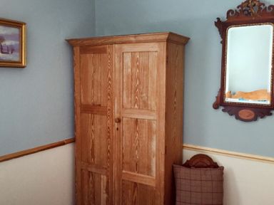 A wooden wardrobe next to a wall with a mirror and a framed painting at Swallow Cottage nr Powburn in Powburn