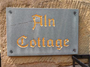 A stone plaque with the text Aln Cottage mounted on a brick wall at Aln Cottage Alnwick