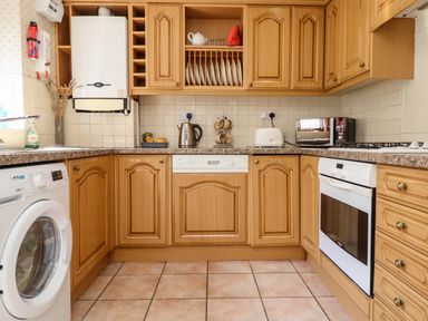 A kitchen with wooden cabinets a washing machine a kettle a toaster a microwave and a built in oven at Aln Cottage Alnwick