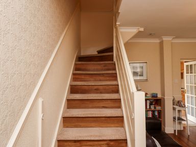 A staircase with carpeted steps and wooden risers next to a living area with a bookshelf and a picture frame at Aln Cottage Alnwick