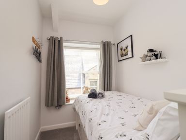 A small bedroom with a single bed next to a window with grey curtains and a picture of sheep on the wall at Aln Cottage Alnwick