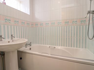 A bathroom with a sink and bathtub with striped and bow patterned tiles at Aln Cottage Alnwick