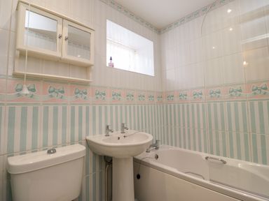 A bathroom with a toilet sink and bathtub with patterned tiles at Aln Cottage in Alnwick