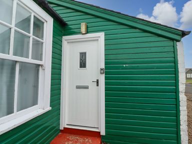 A green exterior wall with a white door and window at Armstrong Cottages No2 in Bamburgh