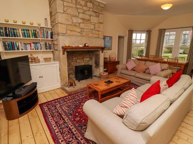 A living room with sofas and pillows around a wooden coffee table and a stone fireplace with bookshelves at Armstrong Cottages No2 Bamburgh