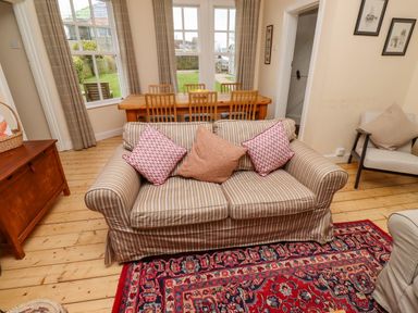 A living room with a striped sofa and cushions in front of a dining table with wooden chairs at Armstrong Cottages No2 Bamburgh