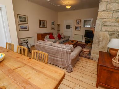 A living room with striped sofas red cushions wooden table and tv near a stone wall at Armstrong Cottages No2 in Bamburgh