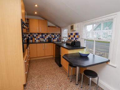 A kitchen with wooden cabinets a black countertop a small dining table with stools and tiled backsplash at Armstrong Cottages No2 Bamburgh
