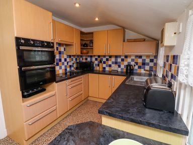 A kitchen with wooden cabinets black appliances and blue and yellow tiled backsplash at Armstrong Cottages No2 in Bamburgh