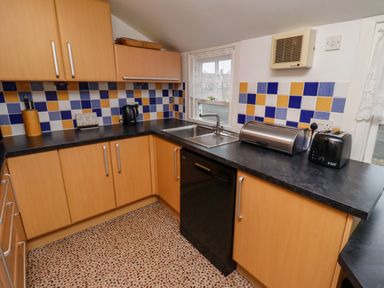 A kitchen with wooden cabinets a black countertop a sink a toaster a kettle and a tiled backsplash at Armstrong Cottages No2 in Bamburgh