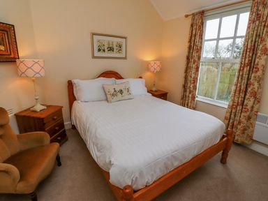 A bedroom with a wooden bed white bedding bedside tables with lamps a window with floral curtains and an armchair at Armstrong Cottages No2 Bamburgh
