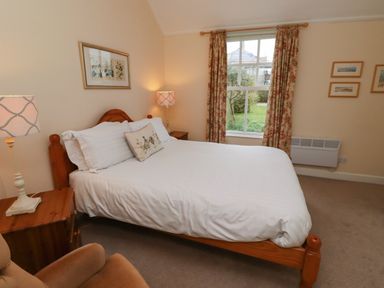A bedroom with a wooden bed and white bedding next to a window with floral curtains at Armstrong Cottages No2 in Bamburgh