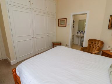 A bedroom with a bed a chair built in wardrobes and a view into a bathroom at Armstrong Cottages No2 in Bamburgh