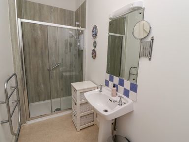 A bathroom with a shower enclosure sink with mirror wicker drawer unit and towel rack at Armstrong Cottages No2 in Bamburgh