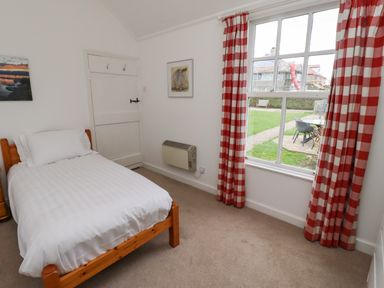 A bedroom with a single bed wooden frame and white bedding red check curtains on window at Armstrong Cottages No2 Bamburgh