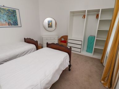 A bedroom with two single beds a white dresser a round mirror an open wardrobe and a wicker chair at Armstrong Cottages No2 Bamburgh