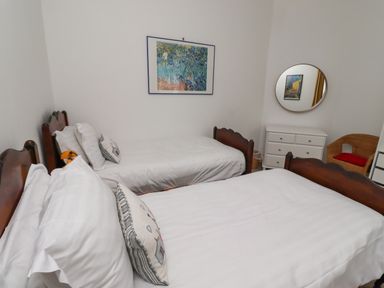 A bedroom with two single beds a white dresser with a round mirror and a wicker chair at Armstrong Cottages No2 in Bamburgh