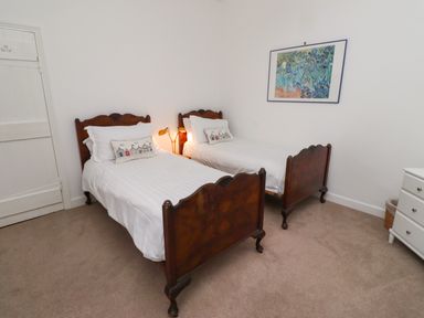 A bedroom with two single wooden beds with white linens a bedside lamp a white chest of drawers and a framed painting on the wall at Armstrong Cottages No2 in Bamburgh
