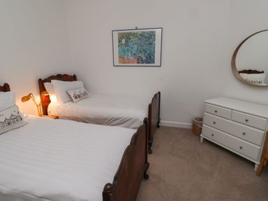 A bedroom with two single beds with wooden headboards a white dresser with drawers a round mirror on the wall and a painting above one bed at Armstrong Cottages No2 in Bamburgh
