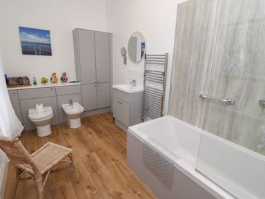 A bathroom with a bathtub a sink toilet bidet wicker chair and grey cabinets at Armstrong Cottages No2 Bamburgh