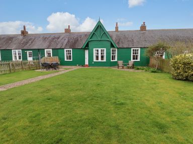 A green exterior cottage with a lawn and outdoor seating at Armstrong Cottages No2 in Bamburgh