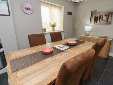 A dining area with a wooden table and four brown chairs at Assisi Apartment in Alnmouth