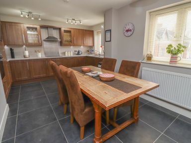A kitchen with wooden cabinets a wooden dining table with four chairs and a window with blinds at Assisi Apartment in Alnmouth