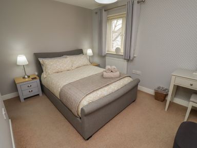 A bedroom with a double bed nightstands lamps a window desk and a chair at Assisi Apartment in Alnmouth