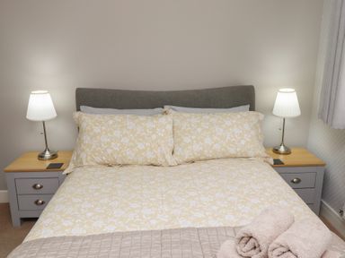 A bedroom with a bed covered with floral bedding two bedside tables with lamps and rolled towels on the bed at Assisi Apartment in Alnmouth