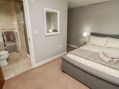 A bedroom with a bed and bedside table with lamp and an adjoining bathroom at Assisi Apartment in Alnmouth