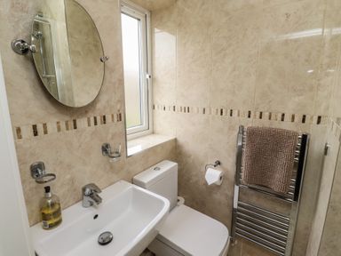 A bathroom with a sink mirror toilet window and towel rack at Assisi Apartment in Alnmouth