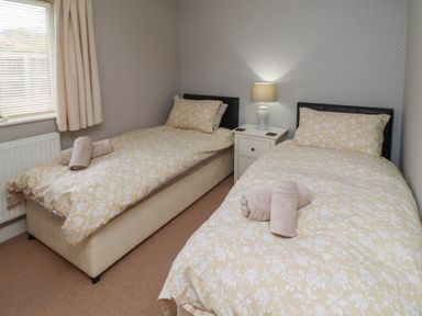 A bedroom with two single beds with yellow floral bedding and towels on them at Assisi Apartment in Alnmouth