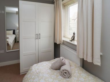 A bedroom with a bed, white wardrobe, window with blinds and curtains, and a mirror showing part of another bed at Assisi Apartment in Alnmouth
