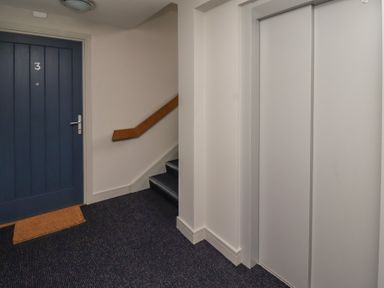 A hallway with a blue door numbered 3 a staircase with a wooden handrail and an elevator with closed silver doors at Assisi Apartment in Alnmouth